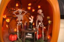an orange pumpkin with greenery and bark, pumpkins, pumpkin lights and skeletons at a table is a fun idea