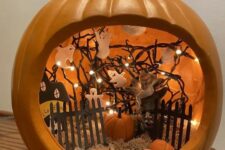 an orange pumpkin with hay, a fence, a paper house, ghosts attached to the lights and small pumpkins