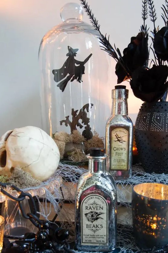 catchy Halloween decor with vintage posion bottles, skulls, candleholders, a cloche with a witch scene and a black vase with black blooms