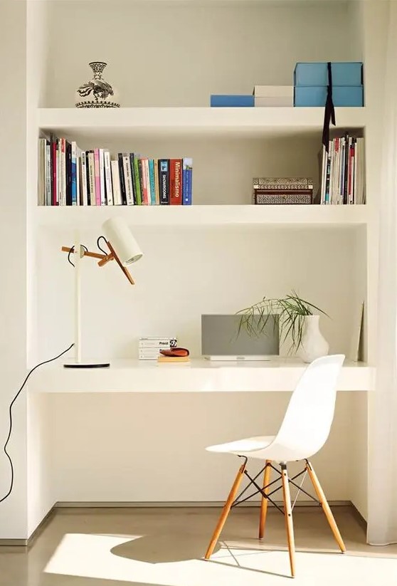 modern niche with shelves and a desk, books, a table lamp, some greenery and boxes for storage, a white chair
