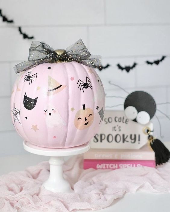 a cute light pink pumpkin with painted cats, ghosts, pumpkins, spiders and a black bow on top is amazing for Halloween