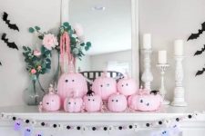 a Halloween mantel with pink pumpkins with googly eyes, banners with ghosts and bats, blooms and candles in white candleholders