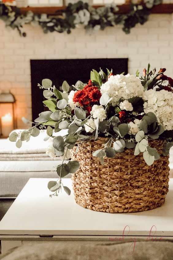 a beautiful fall flower arrangement in white and burgundy and greenery placed into a basket for a farmhouse feel