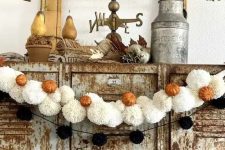 a black pompom and white pompom Halloween garland with little orange pumpkins is great not only for Halloween but also for the fall