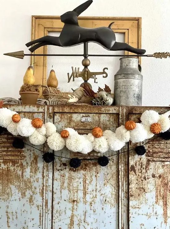 a black pompom and white pompom Halloween garland with little orange pumpkins is great not only for Halloween but also for the fall