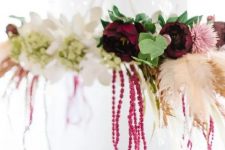 a boho fall chandelier of burgundy, white and pink blooms and spray painted feathers for decor