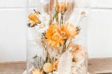 a bold dried flower arrangement in a cloche, with orange and neutral dried blooms, herbs and a bit of greenery is a cool centerpiece