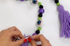 a bright Halloween garland with purple, green and black balls and monster eyes plus purple tassels can be made for Halloween yourself