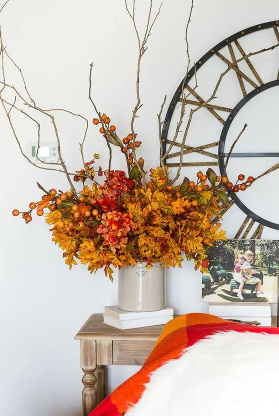 a bright and fun fall centerpiece of orange leaves, red blooms, branches with berries is a stylish idea