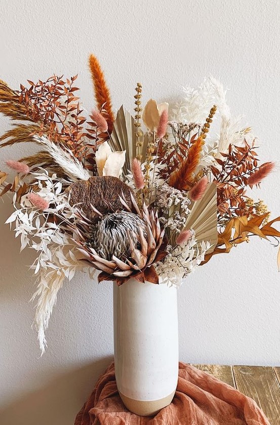 a bright boho Thanksgiving centerpiece with dried leaves, bunny tails and various blooms and fronds