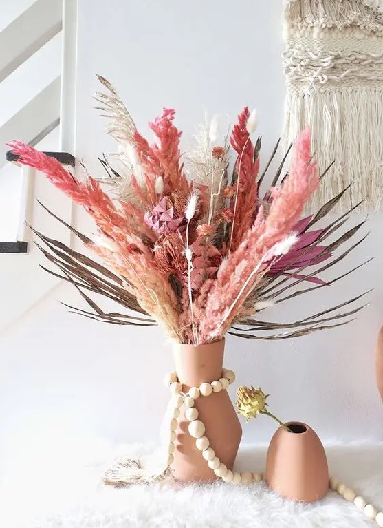a bright dried flower and grass centerpiece of a terracotta vase, bright fronds, leaves and grasses and plus some flowers