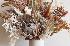 a bright fall dried flower arrangement with a king protea, grasses, leaves and some blooms done in pink, rust and white