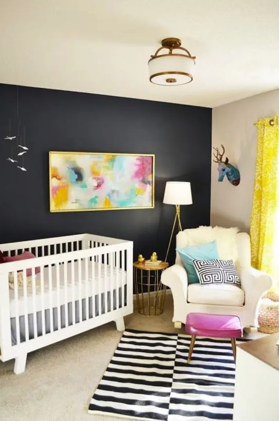 a bright mid-century modern nursery with a black accent wall, white furniture, layered rugs, a bright artwork and some pillows, a pink pouf