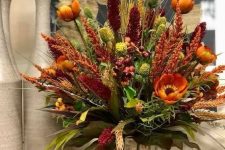 a bright rustic arrangement of rust, burgundy faux blooms, dried herbs and greenery and wooden sticks in the vase