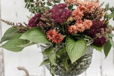 a chic and bold fall flower arrangement in burnt orange and burgundy, with leaves, is a cool and colorful decoration