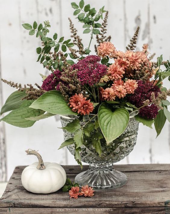 a chic and bold fall flower arrangement in burnt orange and burgundy, with leaves, is a cool and colorful decoration