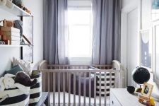 a chic tiny nursery with a stained crib, a white dresser and a black one, a striped rug and printed bedding, a wall-mounted shelf and toys