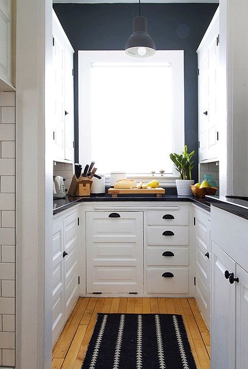 a contrasting U-shaped kitchen with white cabinetry, navy walls, black fixtures and black countertops is super chic