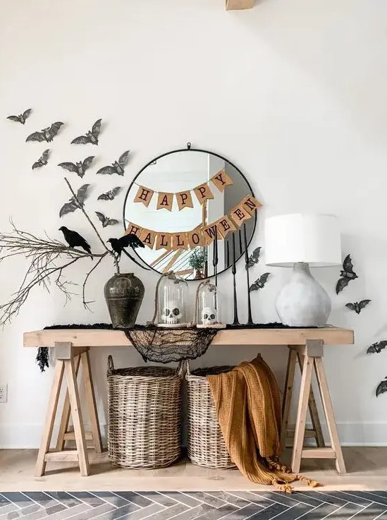a cool Halloween console table styled with black cheesecloth, baskets and blankets, a vase with branches, bats and blackbirds, a couple of banners