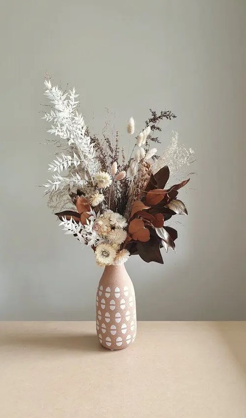 a cool centerpiece of dried blooms, leaves, grasses placed into a printed pink vase is a cool idea for a fall space