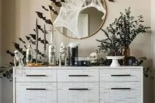 a cool console table with black bats, greenery in vases, skulls and skeletons, spiderwebs is a gorgeous idea for Halloween