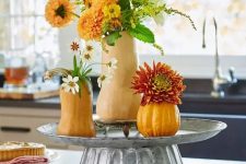 a cool rustic decoration of a metal stand with gourds and pumpkins plus greenery and faux bright blooms