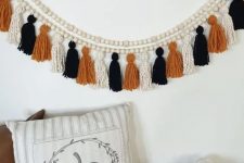 a creative boho Halloween garland of wooden beads, white, orange and black twine tassels is not difficult to make
