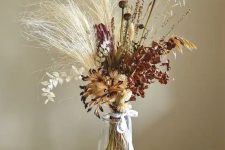 a fall boho centerpiece of grasses, dried blooms and dried leaves and foliage is a pretty and bold decor idea
