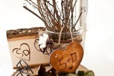a fall centerpiece of a wood slice, moss, greenery, a wooden heart, a wooden piece and some branches and twigs in a glass vase