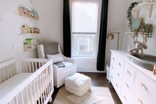 a gender neutral nursery with a neutral crib, a white dresser, a white chair with an ottoman and layered rugs