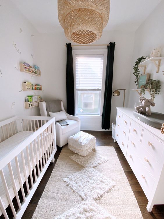 a gender neutral nursery with a neutral crib, a white dresser, a white chair with an ottoman and layered rugs