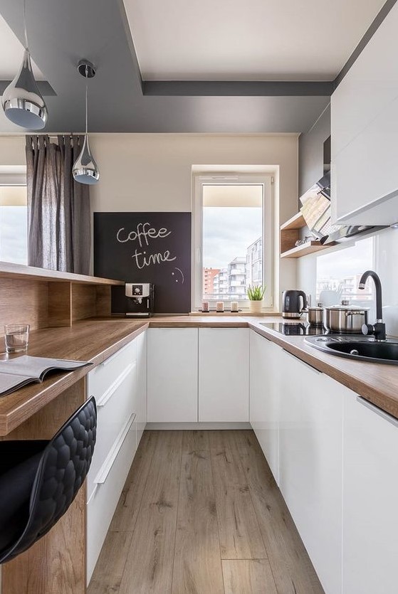 a gorgeous U-shaped kitchen with sleek white cabinets, butcherblock countertops, a chalkboard and black fixtures