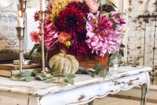a gorgeous and bold fall flower arrangement in burgundy, pink and yellow, with natural greenery and pumpkins around