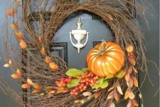 a large textural twig wreath with berries, leaves, greenery and a faux pumpkin is a cool fall decoration