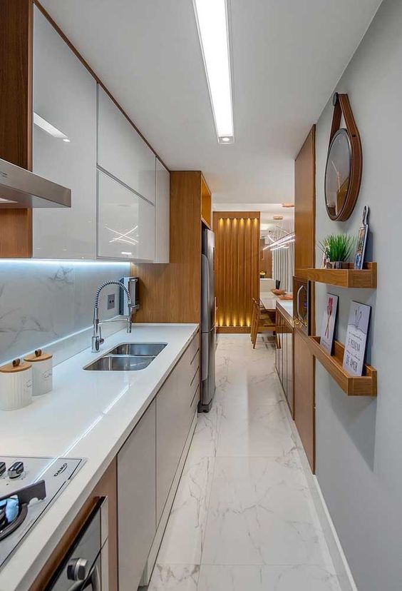 a long narrow kitchen with sleek white and grey cabinets, ledges, built-in lights and some pretty decor