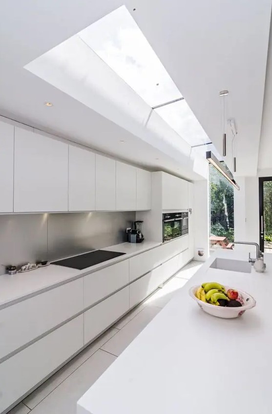 a long narrow minimalist white kitchen with a metal backsplash and skylights to bring much light in