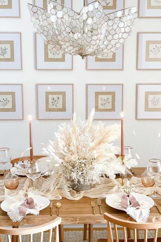 a lovely boho Thanksgiving table setting with a lush dried bloom and grass centerpiece, white porcelain, orange candles and matte cutlery