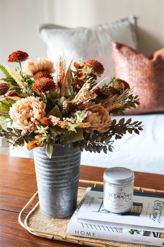 a lovely textural fall floral arrangement in burgundy, rust and blush, with grasses and leaves, placed in a metal bucket