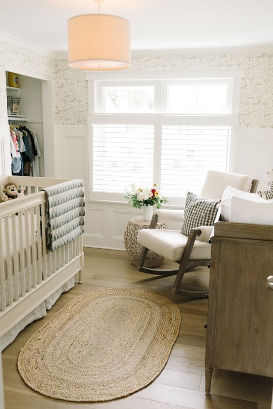 a mid-century modern small nursery with an open closet, a neutral crib, a white chair, a stained dresser and some printed textiles