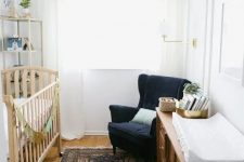 a mid-century modern tiny nursery with a stained crib, a stained dresser, a navy wingback chair, a printed rug and a tall shelving unit