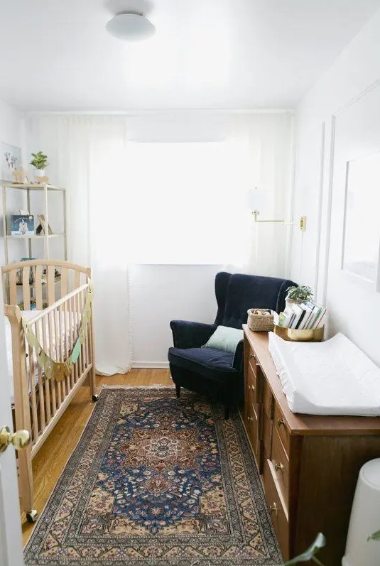 a mid-century modern tiny nursery with a stained crib, a stained dresser, a navy wingback chair, a printed rug and a tall shelving unit