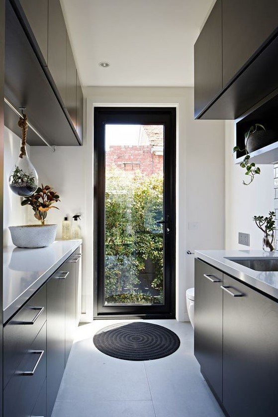 a minimalist black and white kitchen with suspended and usual potted plants, natural light coming through a door