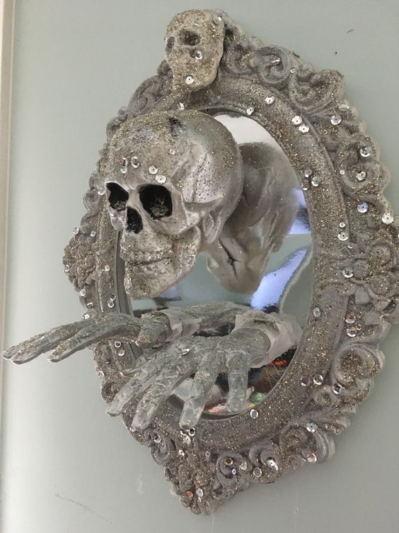 a mirror in a chic glitter and rhinestone frame, with a glitter skull and hands is a cool decor idea for Halloween
