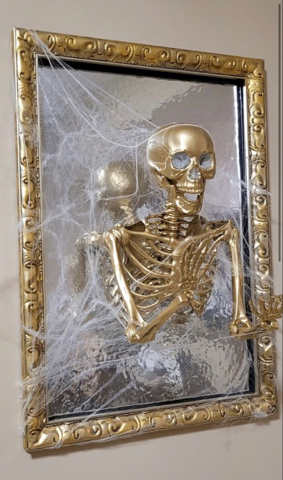 a mirror in a gilded frame and with a gilded skeleton plus spiderweb is a cool and glam decoration for Halloween