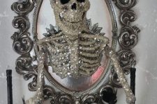 a mirror in a whimsical vintage frame, with a glitter and sequin skeleton coming out of it is a super glam and chic decor idea for Halloween