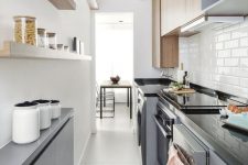 a modern narrow kitchen with sleek grey cabinetry, black stone countertops, open shelves adn stained cabinets, a printed rug