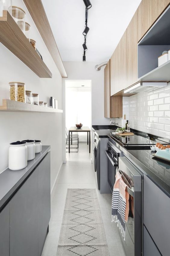 a modern narrow kitchen with sleek grey cabinetry, black stone countertops, open shelves adn stained cabinets, a printed rug
