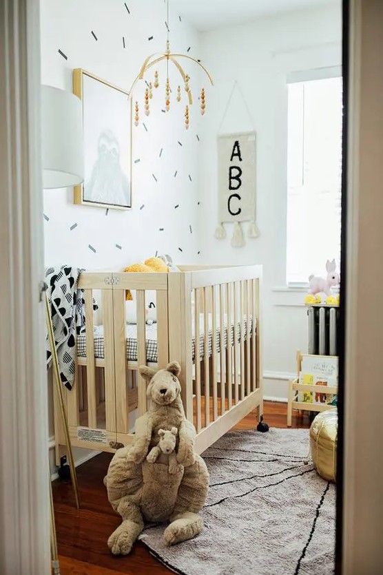 a modern tiny nursery with a stained crib with printed bedding, a changing table, a shelf and some mobiles and toys