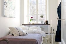 a narrow Scandinavian bedroom with a bed, a windowsill as a storage unit, a stool as a nightstand and some decor