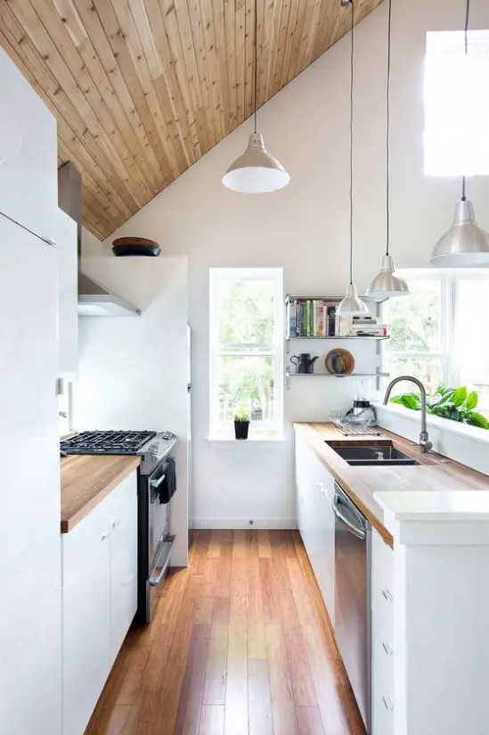 a narrow attic kitchen with white cabinets, butcherblock countertops, pendant lamps and built-in appliances